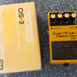 Žlutý kytarový efekt BOSS OS-2 Over Drive/Distortion v originální žluté krabici. Na pedálu jsou čtyři ovládací knoflíky, červená kontrolka CHECK a ná…
