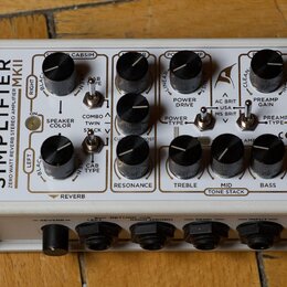 Bílý kytarový zesilovač s nápisem SIMPLIFIER MKII ZERO WATT REVERB STEREO AMPLIFIER. Zařízení obsahuje několik černých otočných potenciometrů a přepí…