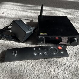 Černý audio přístroj s knoflíkem a anténou, na kterém jsou nápisy TOPPING a DX3Pro. Vedle přístroje je černý napájecí adaptér s kabelem a černý dálko…