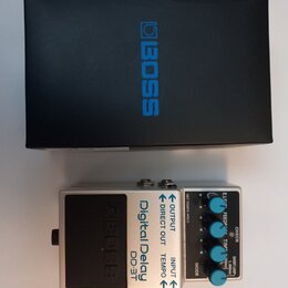 Na fotografii je stříbrný kytarový efekt s nápisy Digital Delay a DD-3T, umístěný před černým krabicem s modrým logem BOSS. Pedal má několik ovládací…