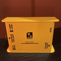 Žlutý kovový box s nápisy Palmer a DACCAPO re-amplification box. Na stranách jsou čitelné popisky BALANCED LINE INPUT s přepínačem -10dBV / +4dBu, LI…