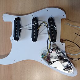 Bílá pickguard pro elektrickou kytaru s třemi černými snímači typu single-coil. K snímačům vedou bílé a černé vodiče, které jsou připojeny k elektron…