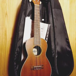 Hnědý ukulele v černé měkké obalu, pod kterým jsou vidět listy s notami. Na hlavě nástroje je nápis "Ohana". Uprostřed těla se nachází štítek s texte…