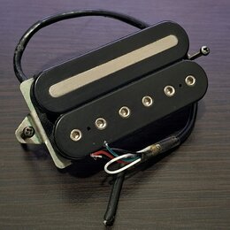 Černý humbucker s dvěma cívkami a kovovým krytem v horní části. Spodní cívka má šest viditelných polových šroubů. Nástroj je umístěn na kovové základ…