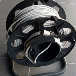 Černý plastový náviják s kovovým spodním rámem, na kterém je namotán šedý kabel. Na kabelu je viditelný konektor. Nástroj nemá žádné viditelné značky…