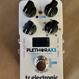 Bílý kytarový efekt s nápisy PLETHORAX1 a TONEPRINT LOADER. Na spodní části je logo tc electronic a nápis TRUE BYPASS. Zařízení má čtyři černé otočné…