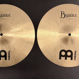 Dvě zlatavé činely z bronzu s viditelným broušením. Oba mají nápisy Byzance a logo MEINL s velkým písmenem M. Na levém činele je text 14" Thin Hihat,…
