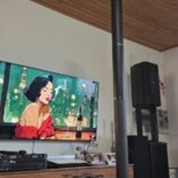 Černý reproduktorový systém složený z vysokého sloupového reproduktoru a subwooferu. Na přední straně subwooferu je bílý nápis JBL. V pozadí jsou vid…