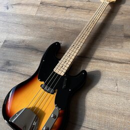 Elektrická basová kytara s tělem v přechodové barvě od žluté po černou a černým pickguardem. Na hlavě hnedku je viditelné logo "Fender". Nástroj má s…