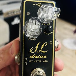 Černý kytarový efekt s zlatým vnitřním rámem a nápisem SL drive BY xotic usa. Na horní straně jsou tři ovládací prvky: otočný knoflík TONE, otočný kn…