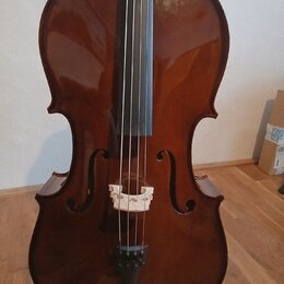 Hnědý smyčkový nástroj, pravděpodobně violoncello, s lakovaným povrchem. Na těle jsou vidět f-otvory, světlá dřevěná kobylka a černý strunník. Nástro…