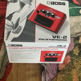 Krabice s červeným vokálovým procesorem značky BOSS, model VE-2 Vocal Harmonist. Na krabici je produktová fotografie zařízení a černobílá fotografie…