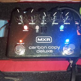 Černý efekt pedál s nápisy MXR a carbon copy deluxe. Na horní straně jsou pětiknobové ovladače s popisky MIX, REGEN, DELAY, SPEED a WIDTH. Jsou zde t…