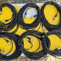 Šest svátků černých audio kabelů s konektory XLR, položených na žlutém povrchu transportního kufru. Kabelové svazky jsou stahnuté černými suchými sta…