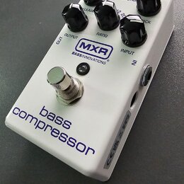Bílý efekt pedál s nápisy MXR BASS INNOVATIONS a bass compressor. Na horní straně jsou čtyři černé otočné ovířky s popisky RELEASE, RATIO, GAIN REDUC…