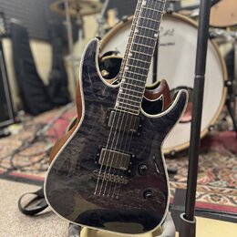 Elektrická kytara s tmavým, žilnatým povrchem těla a hnědými hranami. Nástroj má dva humbuckery s nápisem emo a tři ovládací knofíky. Kytara je umíst…