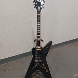 Černá elektrická kytara s tělem ve tvaru hvězdy a chromovanou hlavou. Na hlavě je viditelné logo DEAN. Kytara má dva humbuckery, tři ovládací knoflík…