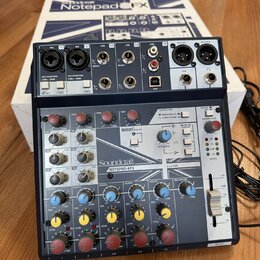 Míchací pult Soundcraft NOTEPAD-8FX v tmavě modré barvě, umístěný před svým původním bílým krabicem s nápisem Notepad 8FX. Na horní straně jsou vstup…
