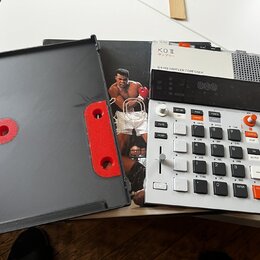Bílý sampler s nápisy K.O II, サンプラー a 64 MB SAMPLER COMPOSER. Zařízení obsahuje numerickou klávesnici, několik posuvníků a ovládacích tlačítek s různ…