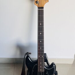 Černá elektrická basová kytara s přírodním dřevěným hmatníkem a hlavou. Na hlavě je nápis Fender MUSTANG BASS. Nástroj má černý plech ochranný kryt (…