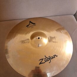 Zlatavý kovový činel s viditelným broušením povrchu. Na činely jsou černé nápisy Zildjian a CUSTOM A, pod kterým je menší text RIDE 20"/0750. Povrch…