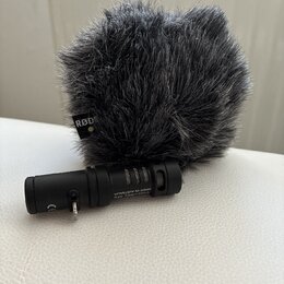 Černý mikrofon s nasazenou šedou chlupatou ochranou proti větru. Na ochraně je viditelné logo RØDE a na těle mikrofonu nápisy Videomic Me MADE IN AUS…