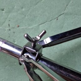 Detail chromovaného kovového stojanu s úhlovým spojem a utahovacím šroubem s knoflíkem. Povrch je lesklý, v místě spoje jsou viditelné drobné škrában…