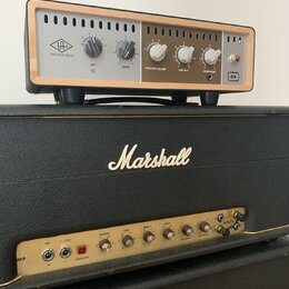 Na fotografii jsou dva kytarové zesilovače. Horní zařízení má stříbrný přední panel s dřevěným rámem, logo UNIVERSAL AUDIO a nápisy RIG, ROOM, SPEAKE…