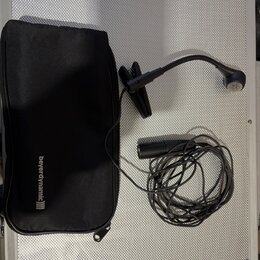 Černý mikrofon s ohebným hrdlem a připojeným kabelem. Vedle něj je černý přepravní pouzdro s bílým nápisem beyerdynamic))). Vše leží na stříbrném pov…