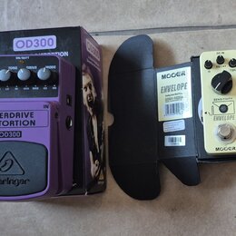 Na fotografii jsou dva kytarové efekty s krabicemi. Fialový pedál má nápisy OVERDRIVE DISTORTION, OD300 a logo behringer. Vedle něj je krémový pedál…