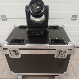 Černý světelný efekt typu moving head umístěný na černé transportní bedně s hliníkovými hranami a úchyty. Na zadním panelu efektu je viditelný disple…