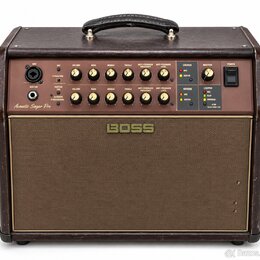Hnědý akustický zesilovač s látkovou mřížkou a koženým úchem. Na předním panelu je nápis Acoustic Singer Pro a v centru mřížky logo BOSS. Ovbední pan…