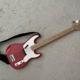 Červená elektrická basová kytara s bílým pickguardem a světlou hnedou hmatníkem. Na hlavě nástroje je viditelné logo "Randy Bass". Kytara má čtyři st…