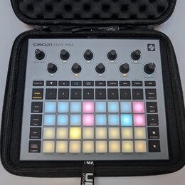 Šedý sampler Novation Circuit Rhythm v černém přepravním pouzdře. Horní část obsahuje osmi otočných ovladačů s popisky jako Master Volume, Start, Sto…