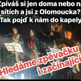 Fotografie zachicuje kapelu čtyř mužů a jedné ženy během hraní na pódiu. Jsou zde vidět elektrická kytara, akustická kytara a bicí souprava. V pozadí…