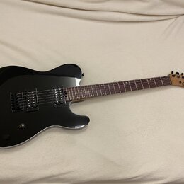 Černá elektrická kytara s tmavým hnedým hmatníkem a světlou dřevěnou hlavou. Na hlavě je viditelné logo Charvel. Kytara má dva humbuckery, jeden ovlá…