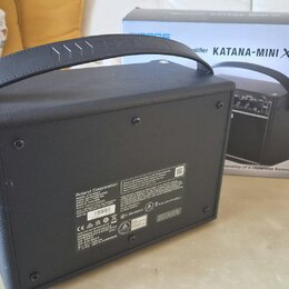 Černý kytarový kombo zesilovač s rukojetí, umístěný vedle původního kartónového obalu. Na krabici je nápis „amplifier KATANA-MINI X“. Na zadní straně…