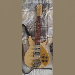 Elektrická kytara s přírodním dřevěným povrchem a hnědým hmatníkem. Nástroj má tři humbuckery, tři ovládací knoflíky a tremolo páku. Na hlavě kytary…