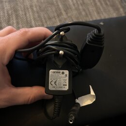 Černý síťový adaptér s napájecím kabelem. Na bílém štítku je uveden nápis BOSS, SWITCHING ADAPTER, MODEL: PSA-100S, INPUT: 100-240V~ 50-60Hz 230mA, O…