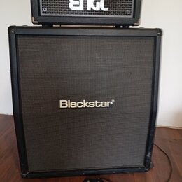 Na fotografii je kytarový zesilovač s boxem. Horní hlava má nápis ENGL a spodní box značku Blackstar. Před boxem na podlaze leží černý dvouknofíkový…