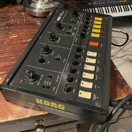 Černý kytarový syntetizér s nápisem KORG GUITAR SYNTHESIZER na spodní hraně. Na horním panelu jsou umístěny různé otočné potenciometry, přepínače a ž…
