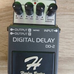Kytarový efekt pedál Digital Delay DD-2 značky Harley Benton v šedém provedení. Na horní části jsou čtyři černé ovládací knoflíky s popisky VEL, MIN…