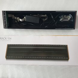 Fotografie zobrazuje černý Eurorack case s vloženým napájecím zdrojem a kabely, vedle jeho původního kartónového obalu. Na krabici je nápis EURORACK…