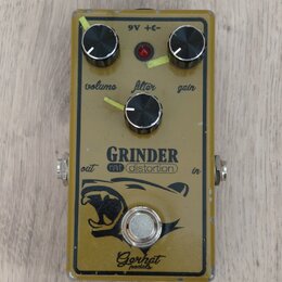 Kytarový efekt pedál v béžovém provedení s černými ovládacími knoflíky. Na povrchu jsou nápisy GRINDER, rat distortion a Gorhat pedals spolu s černým…