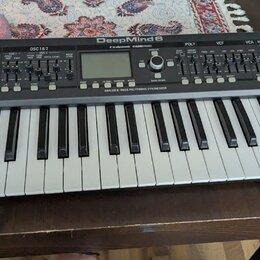 Šedý analogový syntetizátor s klaviaturaí a dřevěnými bočními panely. Na horním panelu je nápis DeepMind 6 a logo tc electronic. Pod ovládacími prvky…