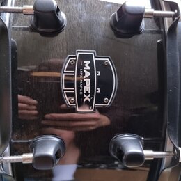 Černý buben s lesklým povrchem a kovovými obručmi. Uprostřed je umístěno logo s nápisem MAPEX a textem MPX MAPLE. Na povrchu jsou viditelné odrazy ok…