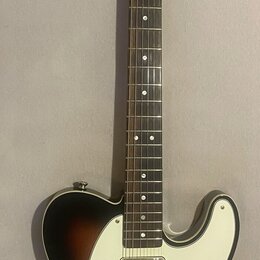 Elektrická kytara s tónem sunburst a bílým pickguardem. Na hlavě hředu je viditelné logo Squier by Fender a nápis CUSTOM TELECASTER. Nástroj je v dob…