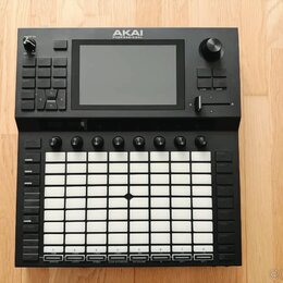 Černý MIDI kontrolér s bílou mřížkou 8x8 gumových padů. Na horní části je umístěn displej a nad ním nápis AKAI PROFESSIONAL. Zařízení obsahuje několi…