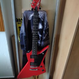 Červená elektrická kytara s ostrovním tvarem těla a hmatníkem z tmavého dřeva. Na hlavě je bílý nápis Aria. Kytara má dva humbuckery, ovládací knoflí…