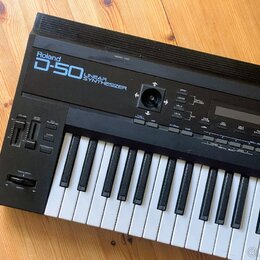 Černý syntetizátor s bílými a černými klávesami. Na horním panelu je nápis Roland D-50 LINEAR SYNTHESIZER. Jsou zde vidět různé ovládací tlačítka, po…